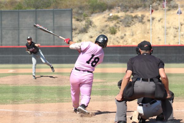 Palomar baseball player in a pink uniform, number 18, swings as the ball flies towards right field.