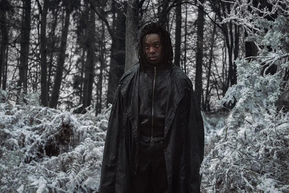 a mysterious figure in a dark outfit standing in a snowy forest