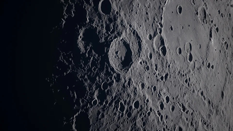 A close up of various craters on the moon's surface, the gray rock in shadow on the left of the image. 