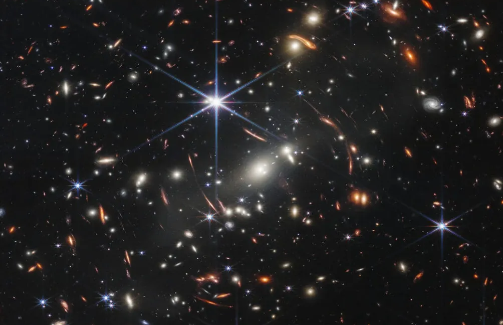 Gravitational lens shows a galaxy just 800 million years post-Big Bang Image of a field of stars and galaxies, with most of them distorted by a gravitational lens.
