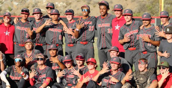 The Palomar baseball team in dark grey uniforms pose for a photo after beating its opponent.