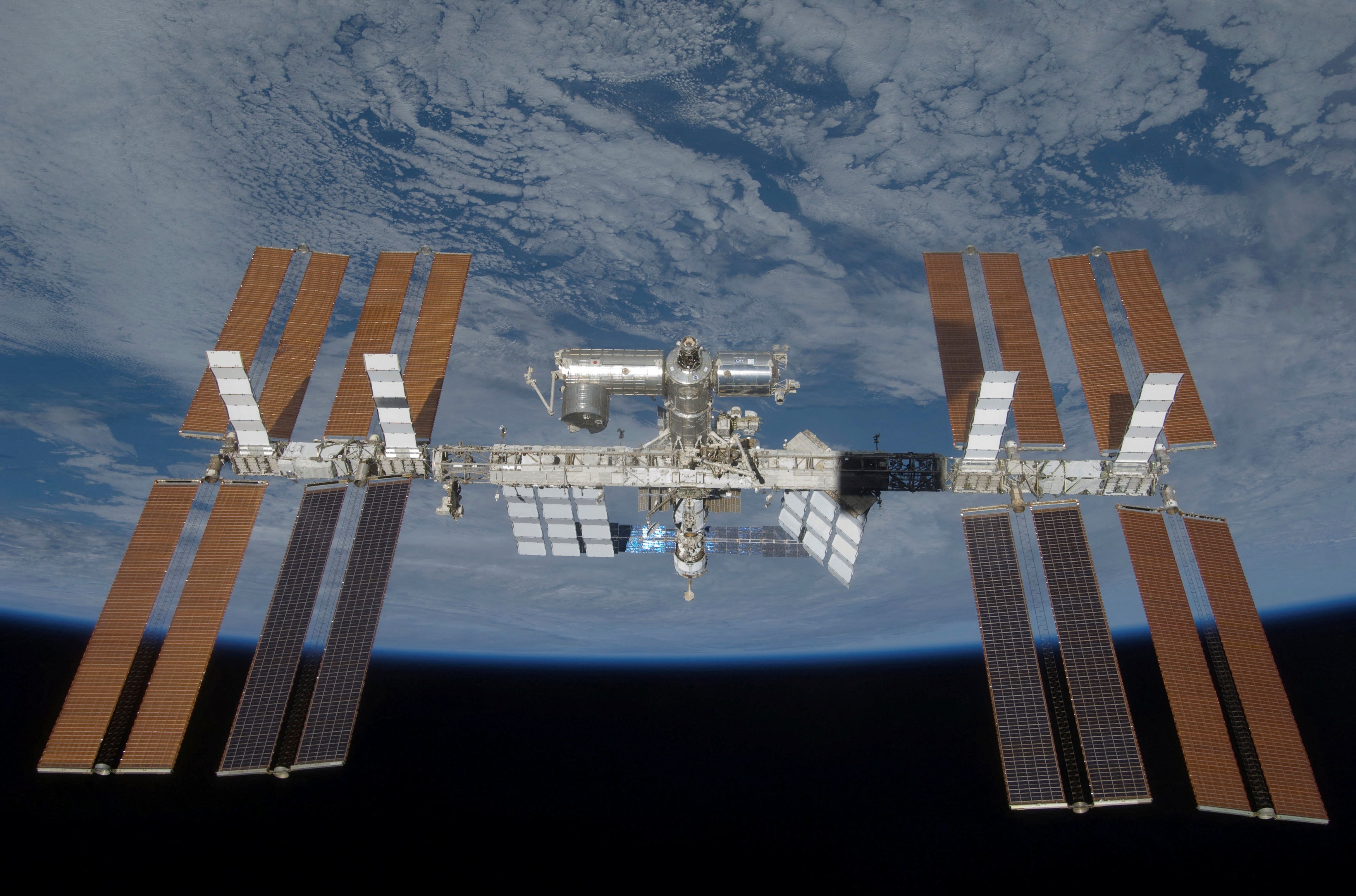 La Estación Espacial Internacional se observa con todos sus paneles solares instalados durante la misión STS-119, con el telón de fondo de la oscuridad del espacio y el horizonte terrestre.