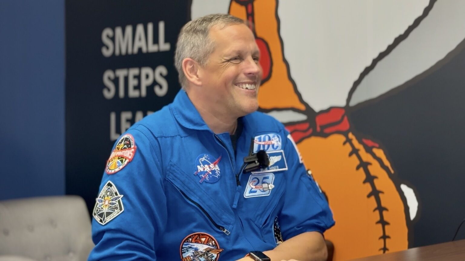 Ever have a scary HR meeting on your calendar? That’s how the Artemis 3 crew found out their assignments A man in a blue jumpsuit sits smiling in front of a wall with a giant snoopy astronaut painted on.