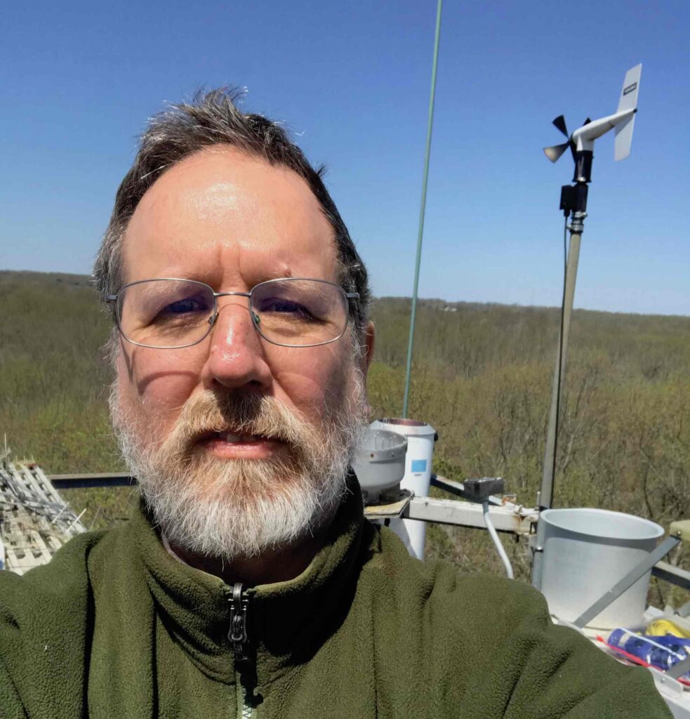 close-up portrait of Fred Huemmrich, weather station and treetops many feet below in the background