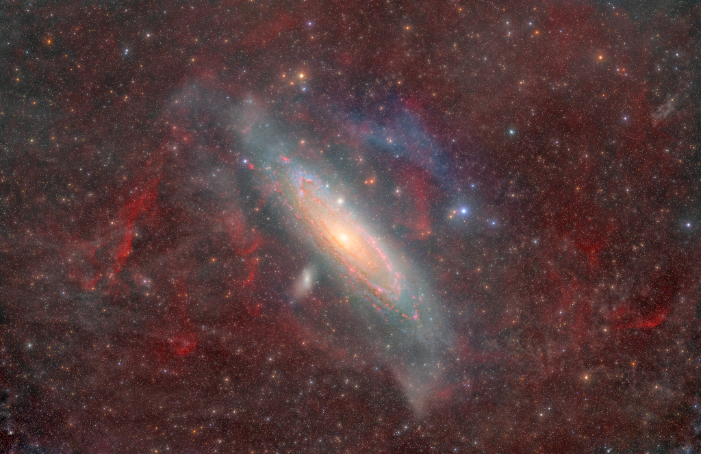 Wispy clouds of dust and gas in the Milky Way obscure the image. Milky Way stars are scattered across the image. Andromeda is a tight spiral of gas, dust, and stars that
occupies the middle background. A couple smaller galaxies look like small bright clumps of stars near Andromeda.