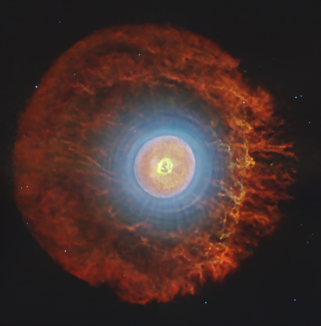 A spherical nebula shows concentric
rings of different colors over a dark
background with a few stars.