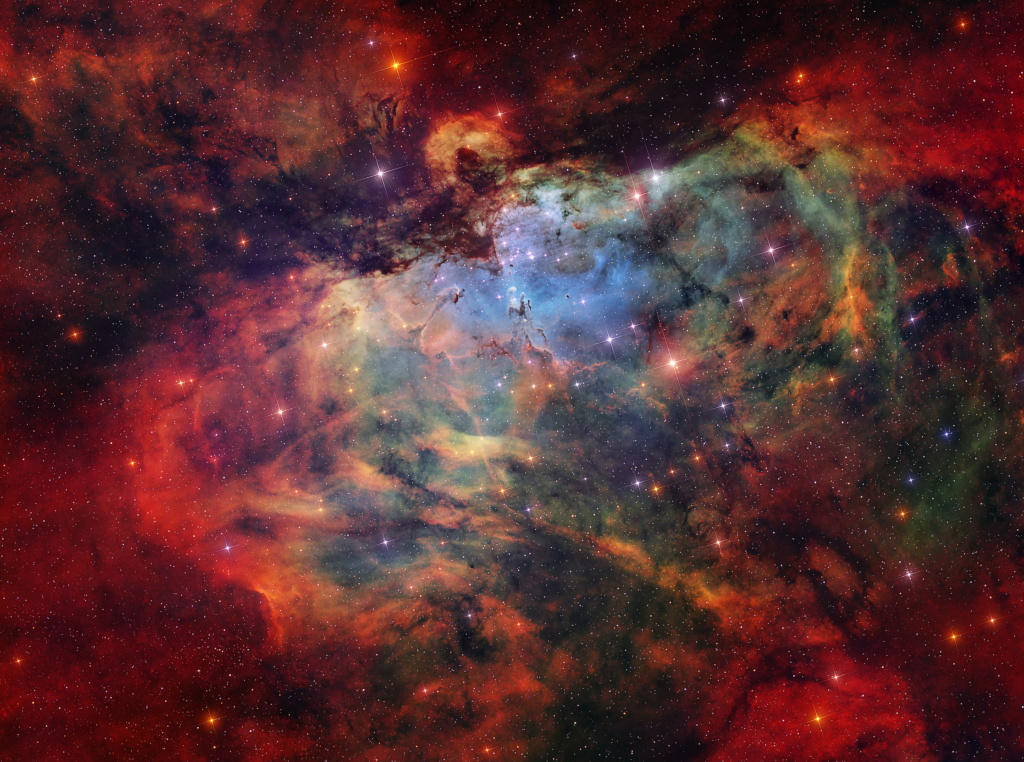 Gas, dust, and stars are scattered across the image. A dark silhouette that looks like an eagle swoops downward towards three small pillars
of gas. Other gas and dust pillar-like features reach out of the surrounding nebula. A central cluster of stars sits beneath the eagle silhouette.