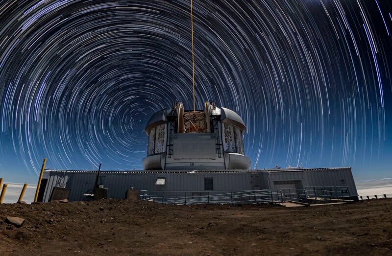 A large observatory telescope under a night sky with circular star trails, created by long-exposure photography, giving a swirling effect around the dome structure.