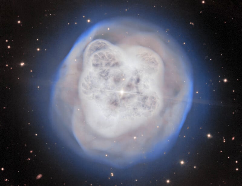 A glowing nebula with a bright central star, surrounded by a cloud of bluish and white gas, set against a dark background filled with small, distant stars.